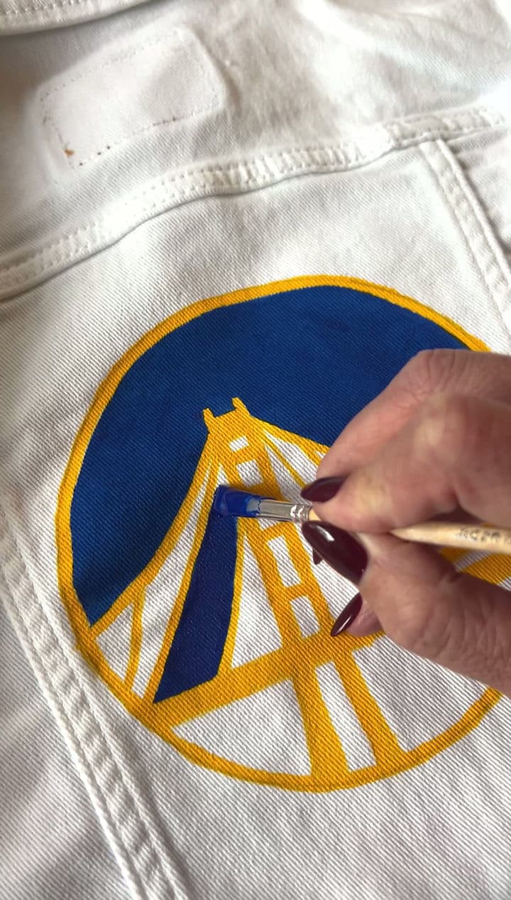 Penelope Jane painting a golden state warriors patch on a denim jacket